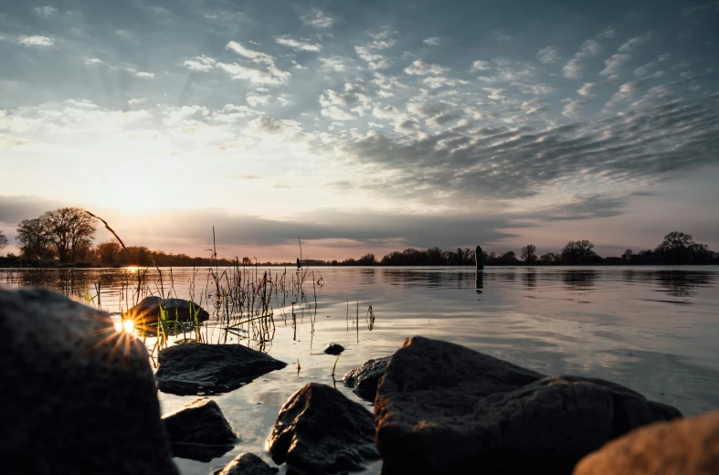 the sun is setting over a body of water, by Sebastian Spreng, pexels contest winner, rocky lake shore, springtime morning, wide view, soft light