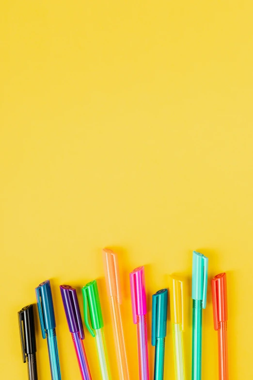 a group of pens sitting on top of a yellow surface, ((neon colors)), no - text no - logo, screensaver, schools