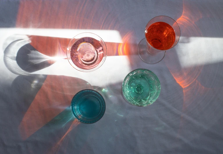 a group of wine glasses sitting on top of a table, inspired by Évariste Vital Luminais, unsplash contest winner, new objectivity, pink and teal and orange, cocktail in an engraved glass, overhead sun, prussian blue and venetian red
