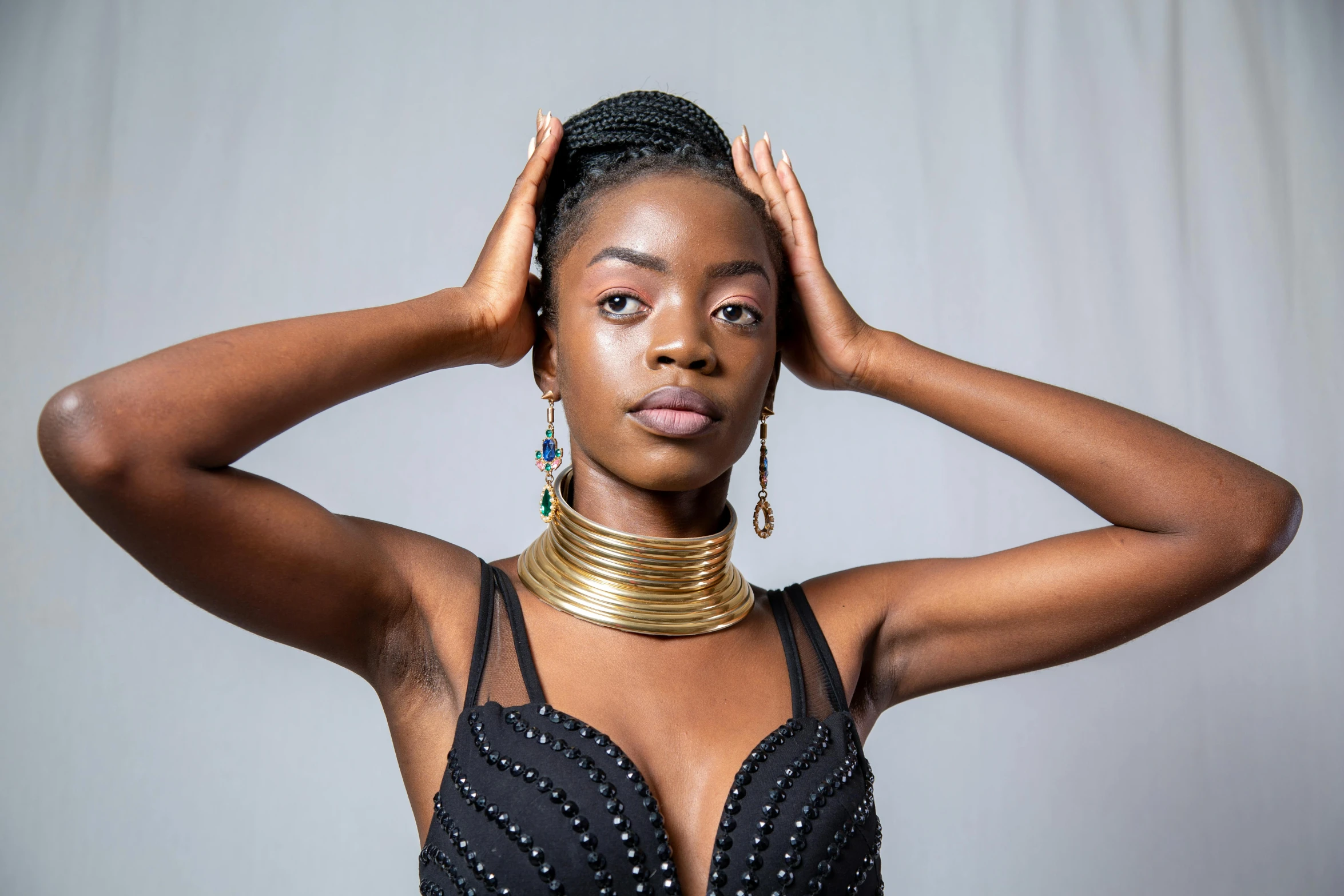 a woman in a black dress posing with her hands on her head, inspired by Ras Akyem, pexels contest winner, afrofuturism, wearing gold detailed choker, metal neck rings, ( ( dark skin ) ), steel choker