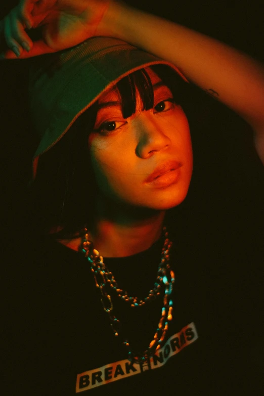 a close up of a person wearing a hat, an album cover, charli bowater and artgeem, dim lighting, neck chains, asian woman