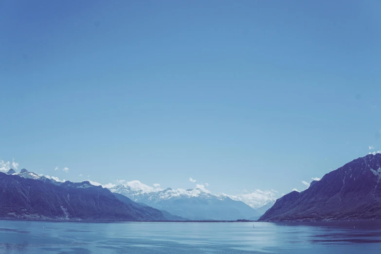 a large body of water with mountains in the background, by Niko Henrichon, pexels contest winner, visual art, clear blue sky vintage style, swiss alps, hd footage, minimalist photo