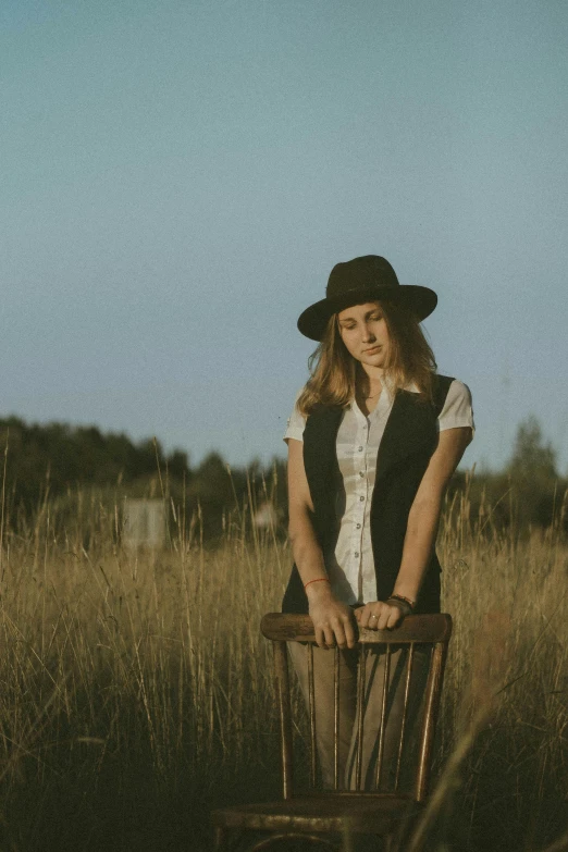 a woman sitting on top of a wooden chair in a field, an album cover, unsplash, wearing a fedora, wearing a vest, portrait image, ekaterina