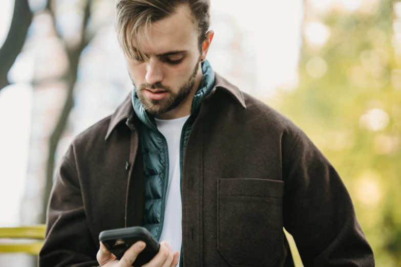 a man looking down at his cell phone, trending on pexels, brown jacket with long sleeves, avatar image, kacper niepokolczycki, rectangle