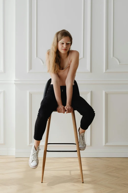 a woman sitting on top of a wooden stool, inspired by Sarah Lucas, trending on pexels, renaissance, sporty physique, sneakers, style of julia razumova, black chair