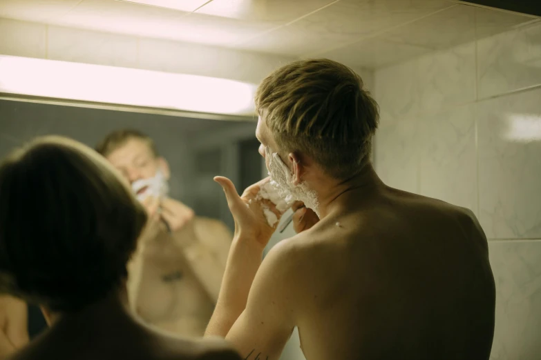 a man shaving his face in front of a mirror, by Elsa Bleda, pexels contest winner, hyperrealism, 1 6 years old, small blond goatee, face and body, evening time