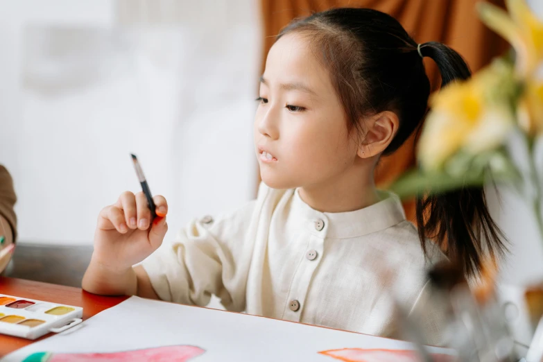a little girl sitting at a table with a cell phone in her hand, a child's drawing, inspired by Qian Xuan, pexels contest winner, visual art, holding a paintbrush in his hand, with a pointed chin, doing an elegant pose, contemplating