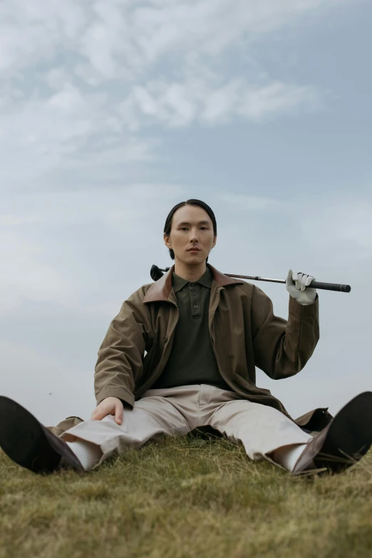 a man sitting on the ground holding a golf club, an album cover, inspired by Fei Danxu, unsplash, androgynous person, inuit, golf course, movie still