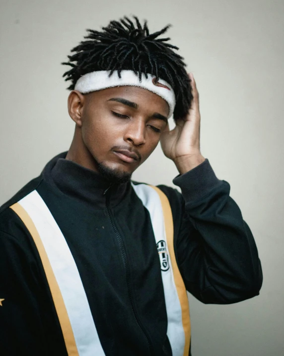 a man with dreadlocks standing in front of a wall, an album cover, trending on pexels, black and yellow tracksuit, androgynous face, cute young man, whitebangsblackhair