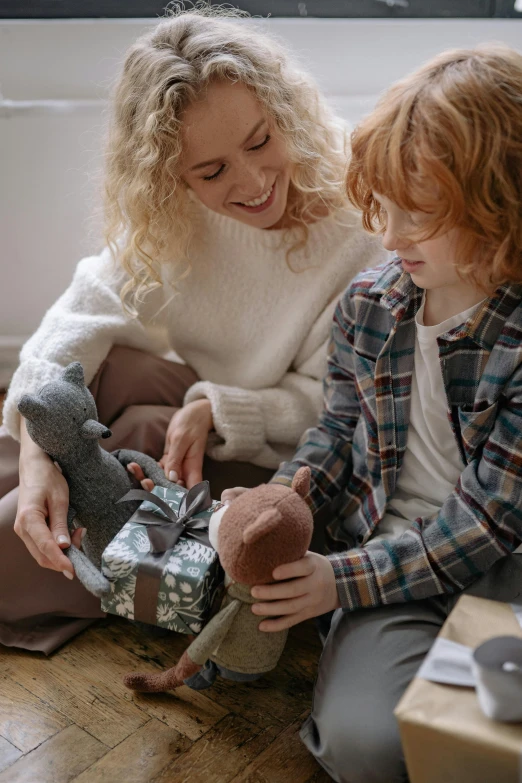 a woman and a child opening presents on the floor, blue'snappy gifts'plush doll, husband wife and son, earthy, grey