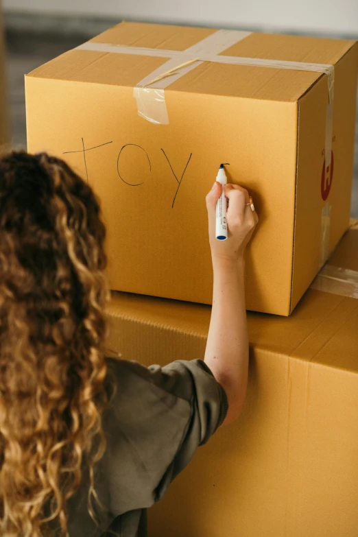 a woman is writing on a cardboard box, trending on pexels, graffiti, toys, avatar image, black marker, gold