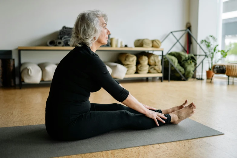 a woman sitting on a yoga mat in a room, a picture, by Helen Stevenson, unsplash, arabesque, older woman, half - turn, profile image, from the front