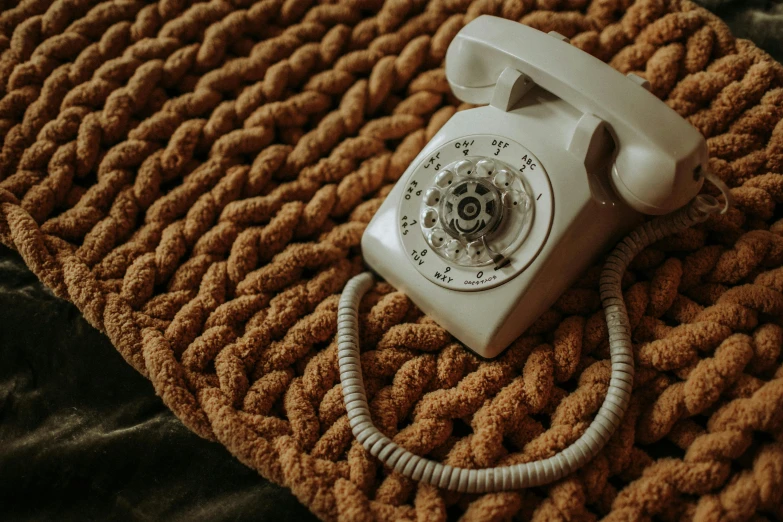 a white telephone sitting on top of a brown blanket, by Carey Morris, trending on pexels, braided cable, 1960s style, rug, dial