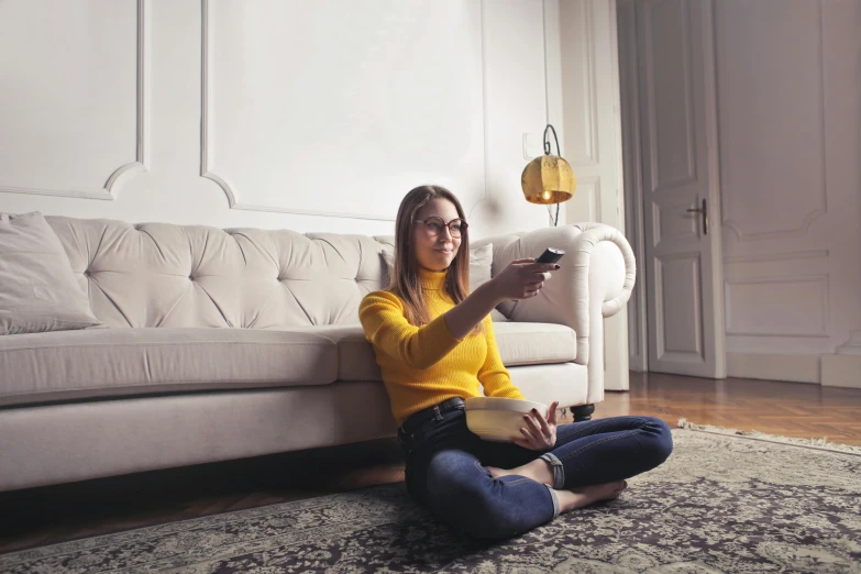 a woman sitting on the floor holding a remote control, pexels, lady using yellow dress, instagram post, watching tv, ad image