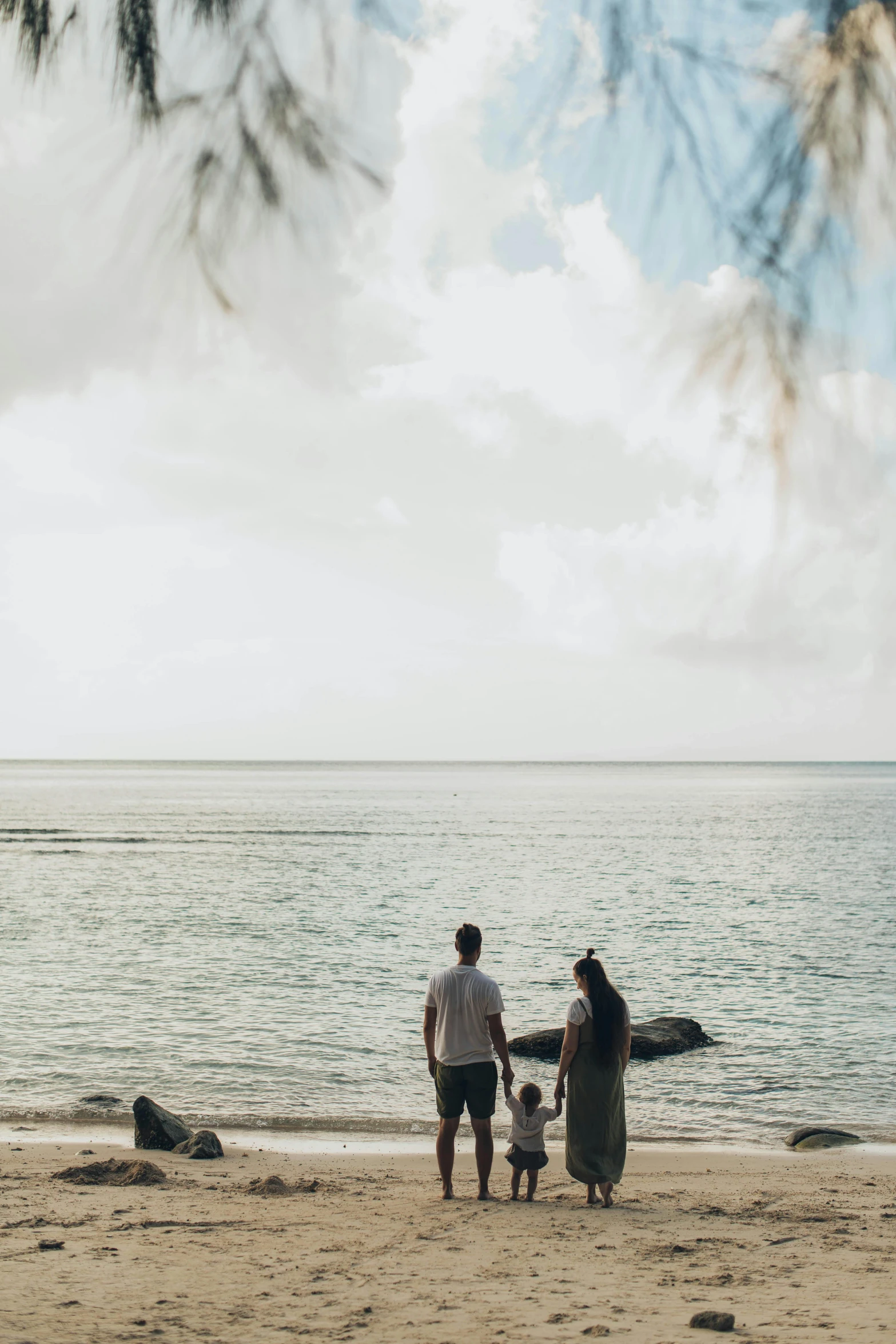 a group of people standing on top of a sandy beach, on the ocean, husband wife and son, unsplash photography, multiple stories