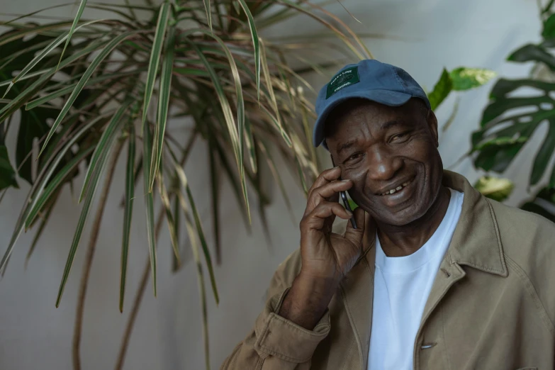 a man talking on a cell phone next to a plant, pexels contest winner, photorealism, black man, old male, smiling for the camera, high resolution product photo
