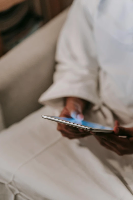 a person sitting on a couch holding a cell phone, wearing a white robe, using a magical tablet, zoomed in, 6 : 3 0 am