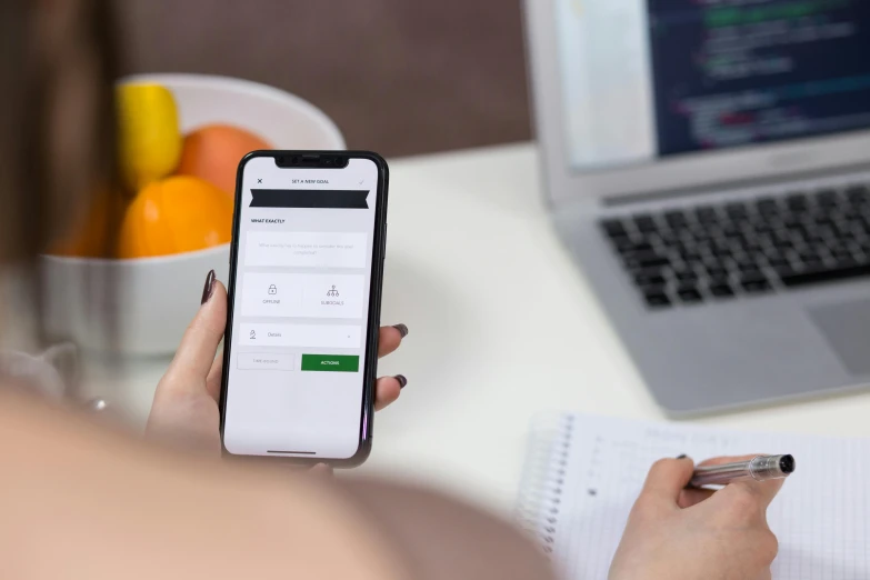 a person holding a cell phone in front of a laptop, well list, on a white table, 9 9 designs, green colored theme