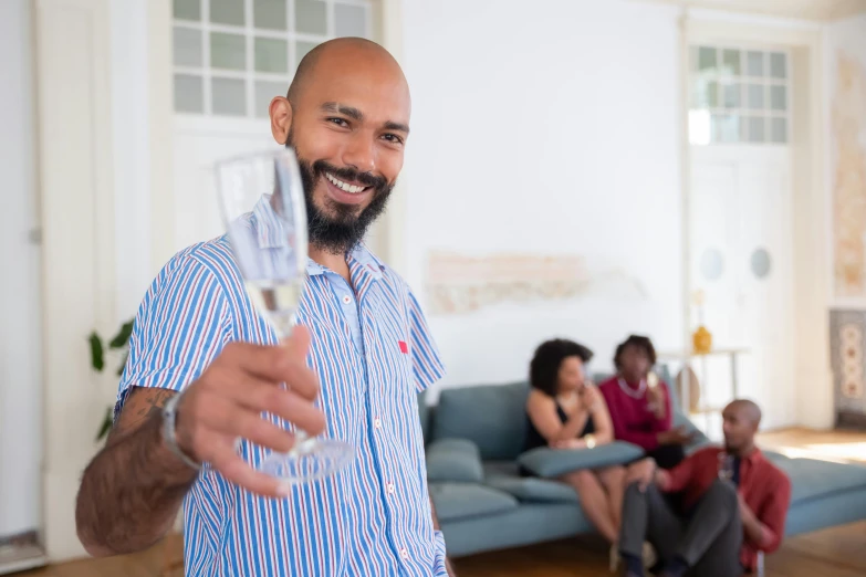 a man holding a glass of wine in a living room, pexels contest winner, brown skin man with a giant grin, champagne commercial, community celebration, standing still