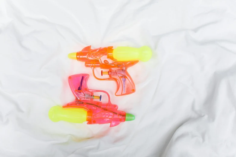 a couple of water guns laying on top of a bed, pexels, ((neon colors)), flat lay, white background, jen atkin