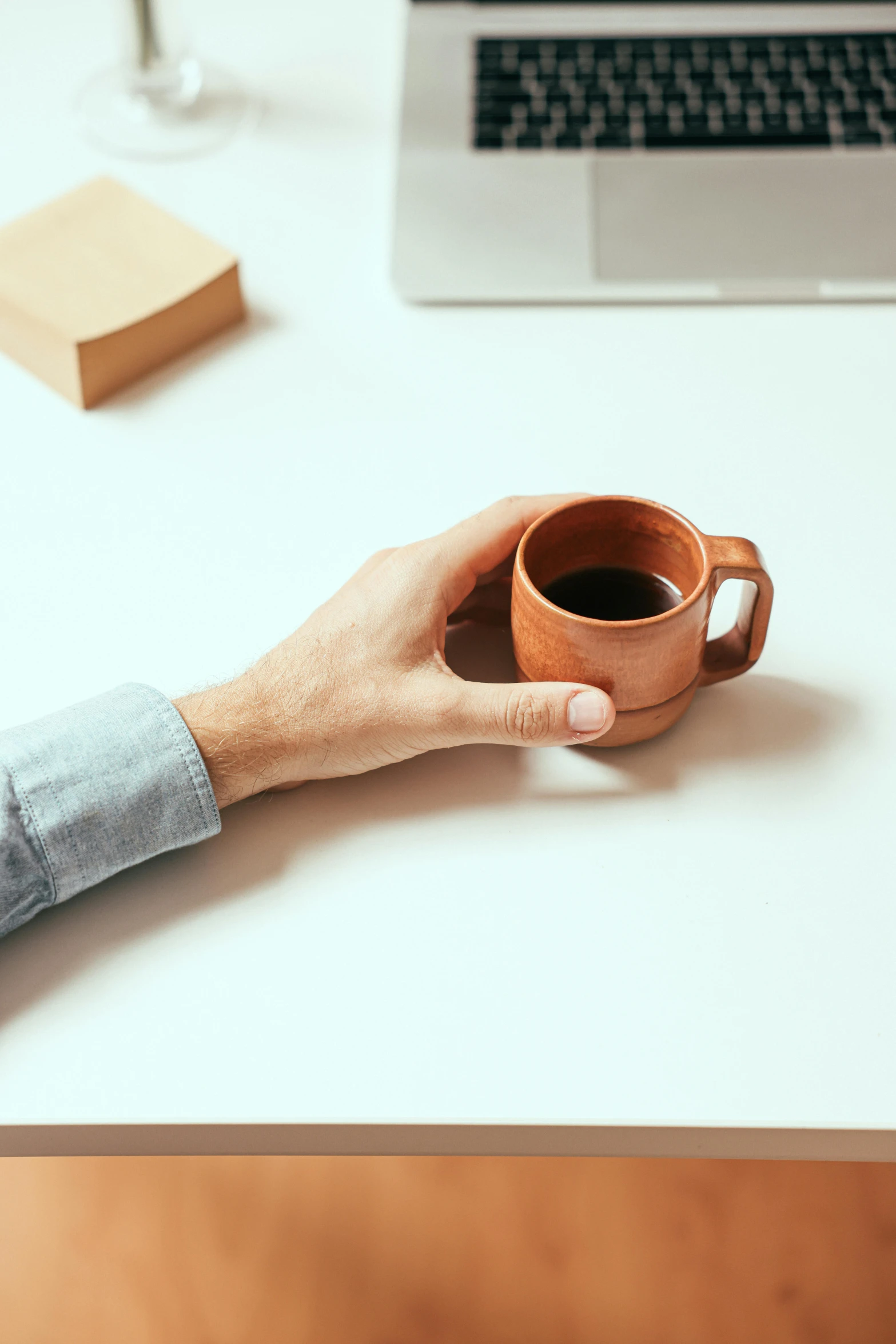 a person holding a cup of coffee in front of a laptop, inspired by Jan Müller, minimalism, sustainable materials, terracotta, product view, small details