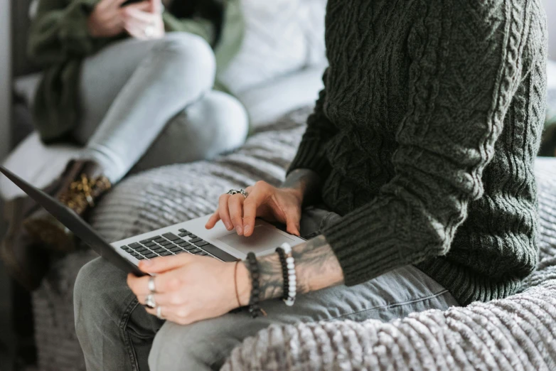 a woman sitting on a couch using a laptop, by Adam Marczyński, trending on pexels, photograph of a sleeve tattoo, couple on bed, wearing a green sweater, heavily detailed