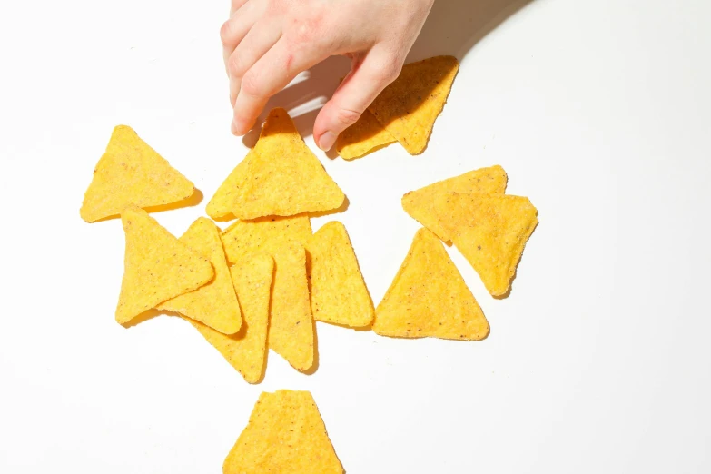 a person reaching for some tortilla chips, by Carey Morris, trending on pexels, process art, on a white table, triangles, rebecca sugar, cheese revolution