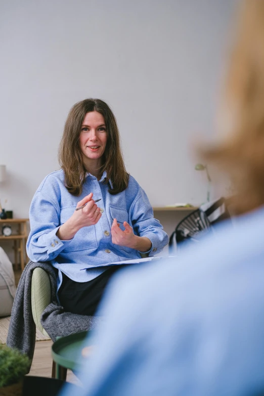 a woman sitting in a chair talking to another woman, wearing a light blue shirt, wide shot photograph, clinical, lena oxton