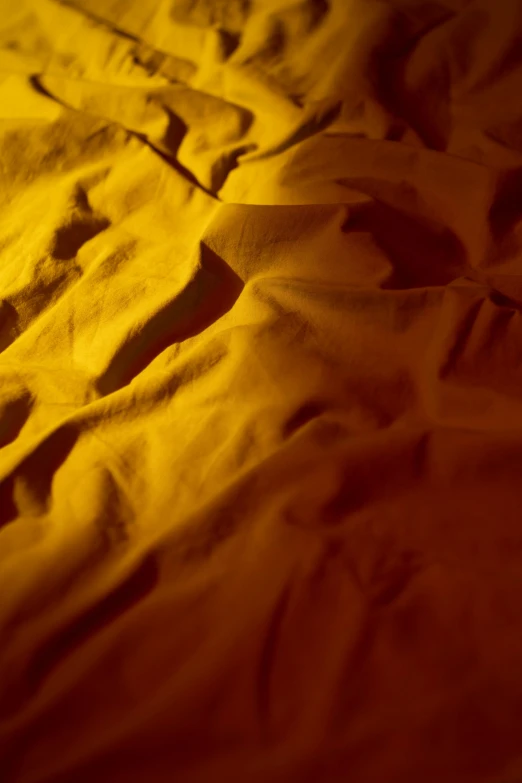 a close up of a blanket on a bed, inspired by Christo, unsplash, lyrical abstraction, shades of aerochrome gold, photographed for reuters, marvelous designer substance, cotton fabric