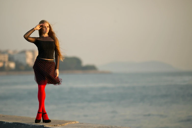 a woman standing next to a body of water, an album cover, inspired by Louisa Matthíasdóttir, romanticism, in red velvet stockings, seaview, backlight photo sample, pr shoot