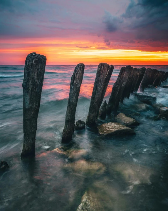 wooden posts sticking out of the ocean at sunset, by Antoni Brodowski, unsplash contest winner, fading rainbow light, looking towards camera, 500px photos, ukraine. photography