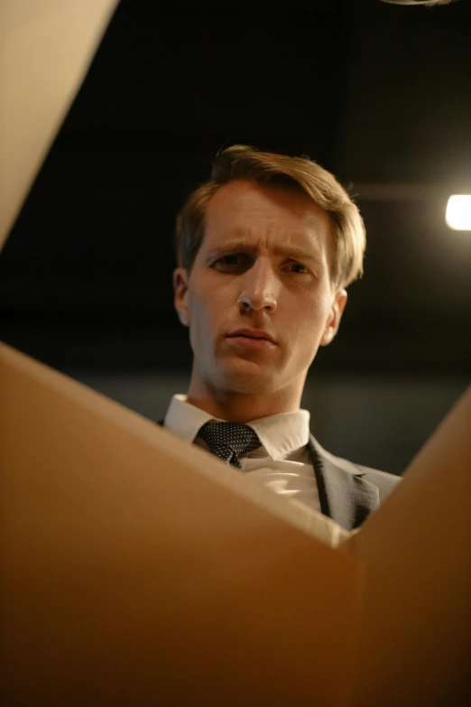 a close up of a person wearing a suit and tie, an album cover, inspired by Oskar Lüthy, he is holding a large book, intense expression, under a spotlight, thumbnail