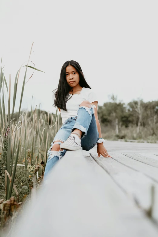 a woman sitting on top of a wooden bench, trending on pexels, ripped jeans, young teen, asian women, in a swamp