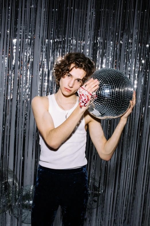 a man holding a disco ball in front of his face, an album cover, by Winona Nelson, renaissance, portrait of timothee chalamet, in a white tank top singing, 2019 trending photo, curly haired