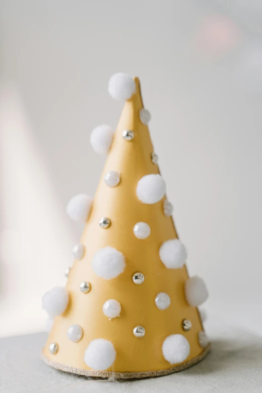 a yellow christmas tree sitting on top of a table, a pastel, unsplash, wearing a party hat, gold and pearls, clay, set against a white background