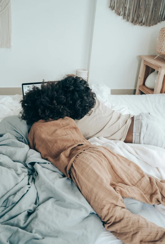 a woman laying on top of a bed covered in blankets, by Cosmo Alexander, trending on pexels, curly afro, facing away, childhood friend vibes, slightly pixelated