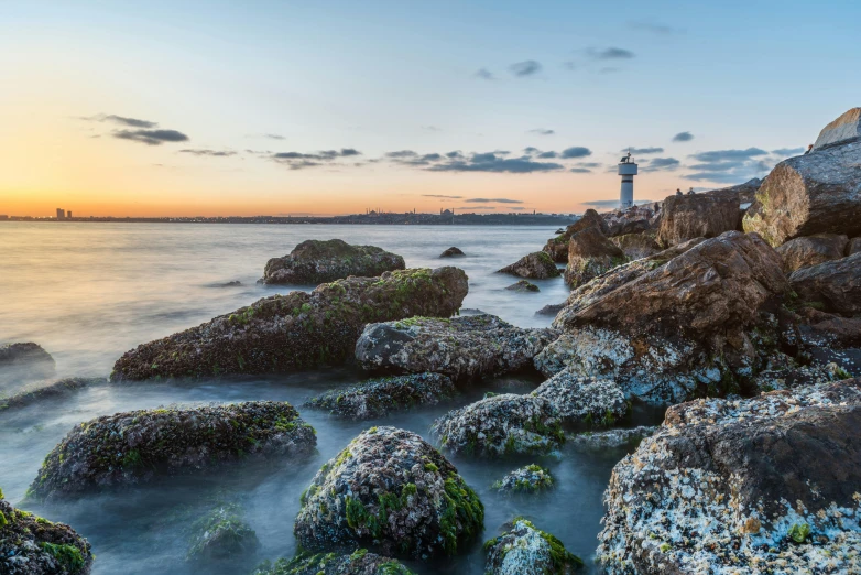 a lighthouse sitting on top of a rocky beach, by Mathias Kollros, pexels contest winner, chiba prefecture, sunset panorama, urban surroundings, shot on sony a 7