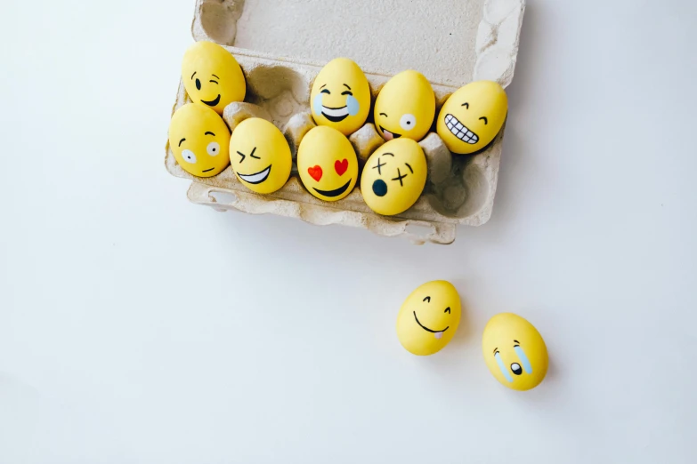 a carton of eggs with smiley faces painted on them, trending on pexels, on a white table, new emoji of biting your lip, taken with sony alpha 9, te pae