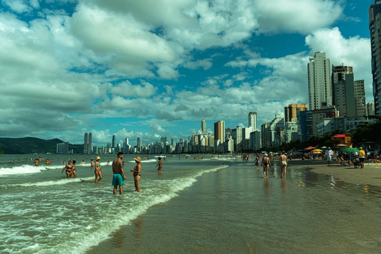 a group of people standing on top of a sandy beach, by Felipe Seade, pexels contest winner, renaissance, avenida paulista, people swimming, thumbnail, clouds and corrupted city behind