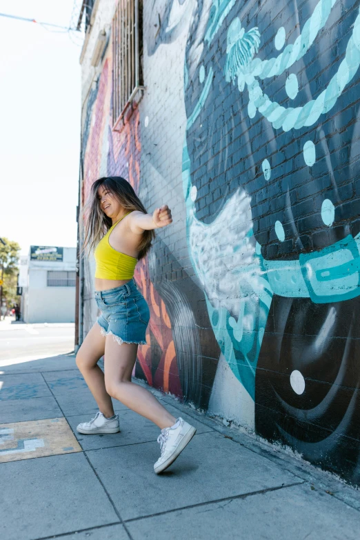 a woman standing in front of a graffiti wall, dance, hollywood promotional image, leslie zhang, sunny day time