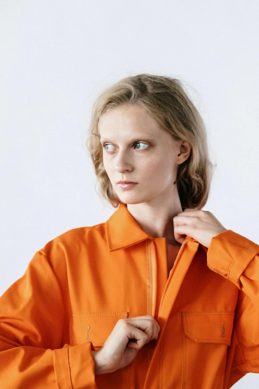 a woman in an orange shirt poses for a picture, an album cover, inspired by Anna Füssli, trending on pexels, prison jumpsuit, attractive androgynous humanoid, lab coat, high resolution image