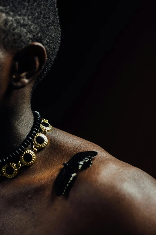 a close up of a person wearing a necklace, an album cover, inspired by Hedi Xandt, trending on pexels, afrofuturism, man is with black skin, wakanda, yasuke 5 0 0 px models, carbon black and antique gold