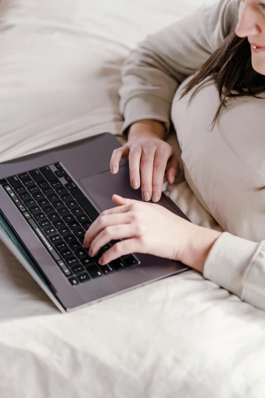 a woman laying on a bed using a laptop computer, pexels, wearing a grey robe, sleek hands, thumbnail, digital image