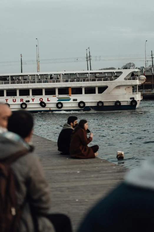 a group of people sitting on a dock next to a body of water, pexels contest winner, hurufiyya, turkish and russian, 🚿🗝📝, they are in love, tiny ships docking