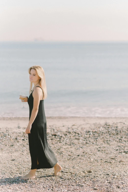 a woman walking on a beach next to the ocean, by Anna Boch, happening, dark black long dress, young blonde woman, seseon yoon, gif