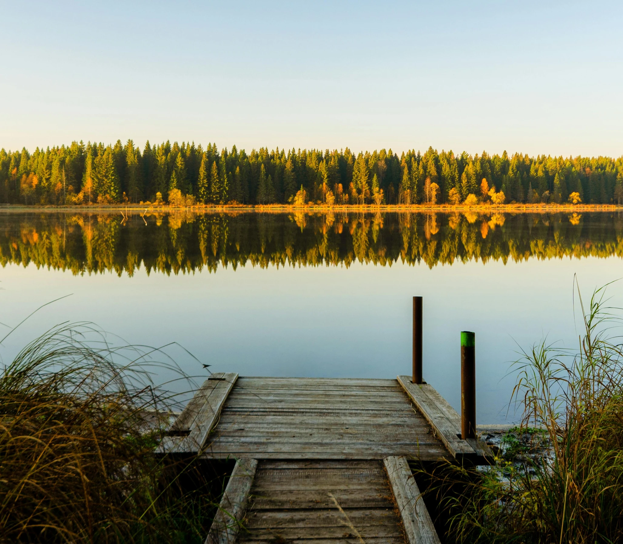 a dock sitting on top of a lake next to a forest, by Jaakko Mattila, pexels contest winner, hurufiyya, soft autumn sunlight, hd footage, ultrawide image, holiday season