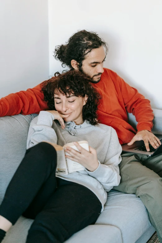 a man and a woman sitting on a couch, pexels contest winner, happening, curly haired, integrating with technology, curled up on a book, red sweater and gray pants