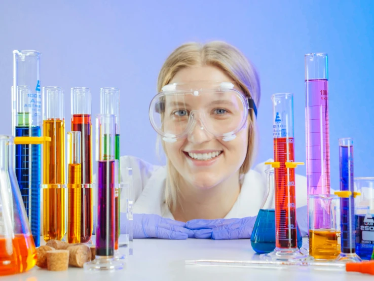 a woman sitting at a table in front of a bunch of test tubes, a portrait, trending on pexels, girl wearing uniform, rainbow liquids, jenny savile, academic clothing