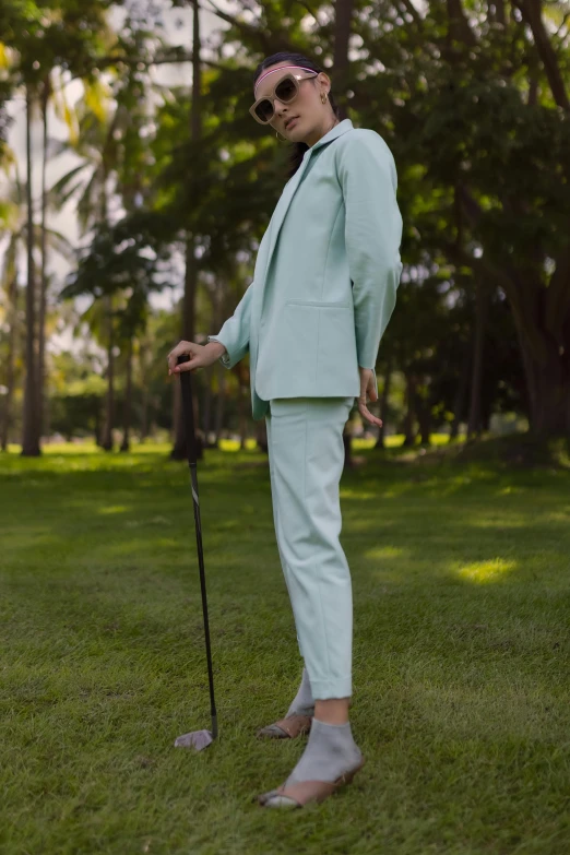 a man standing on top of a lush green field, wearing a light blue suit, holding a cane, in style of thawan duchanee, golf digest