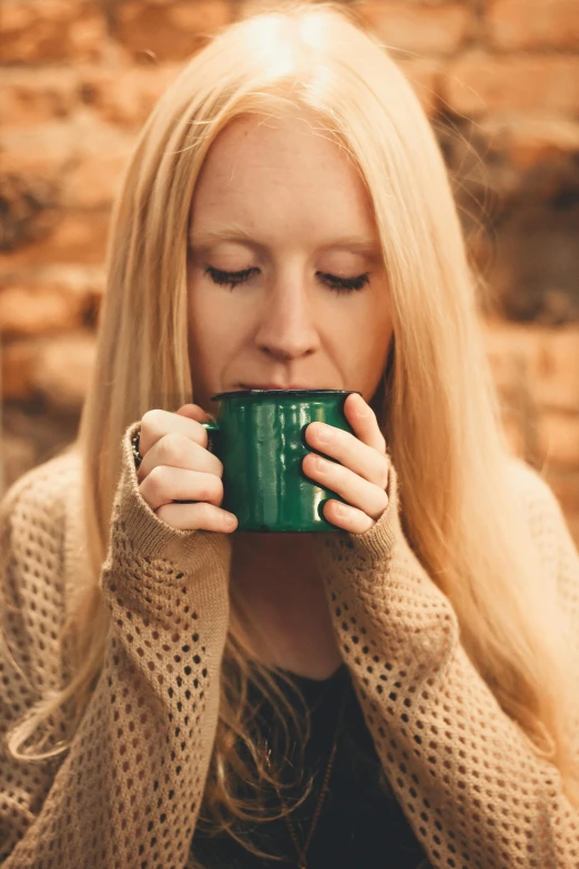 a woman drinking a cup of coffee in front of a brick wall, trending on pexels, renaissance, green and warm theme, blonde swedish woman, ( ( dark green, outdoors